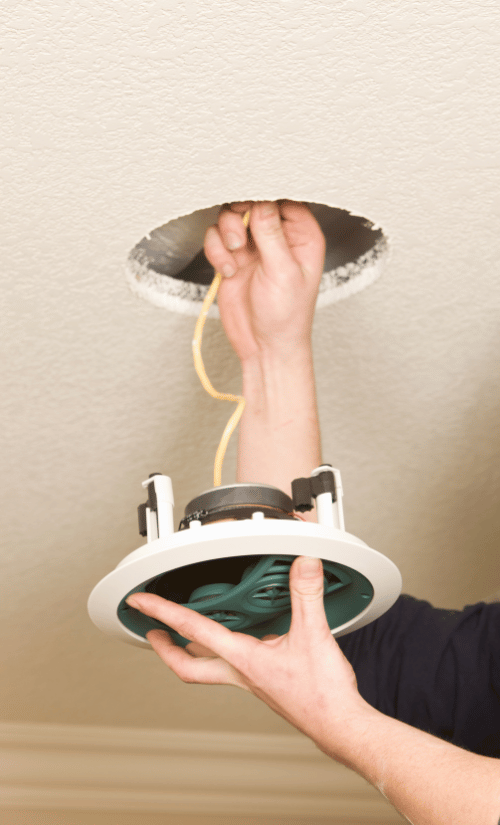 Image of a man fitting a ceiling speaker using the best speaker cable for his system